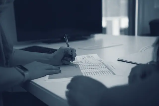 Une main prend des notes sur une feuille imprimée, posée sur une table.