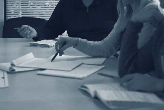 Dues persones assenyalen fulls i notes sobre una taula